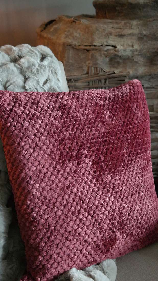 Kussen Rick fluffy in bordeaux met textuurbolletjes, liggend op een zachte deken