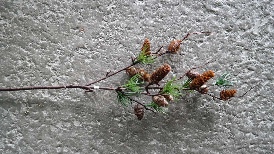 Kunsttak met dennenappels en groene naalden aan een bruine tak