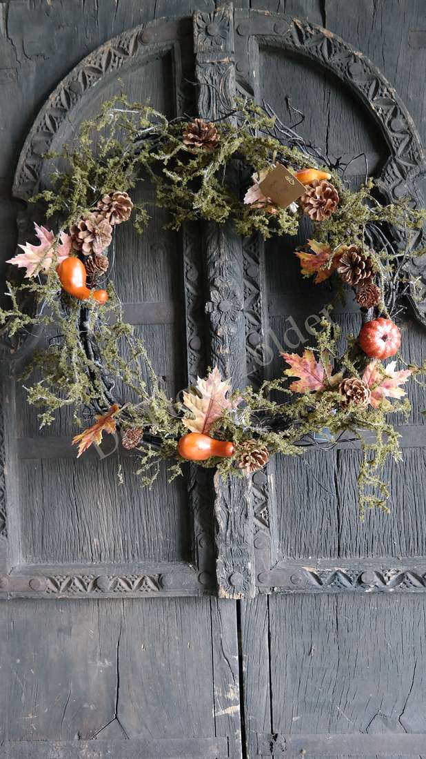 Mos-Herfst krans van De Hooyzolder met dennenappels, oranje pompoenen en mos aan een houten deur.