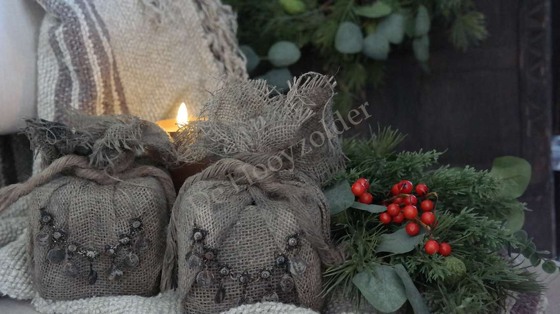Jute cadeau met ketting, naturel burlap zakken, De Hooyzolder, omgeven door groen en rode bessen bij een kaars