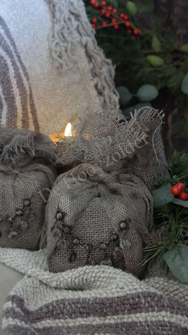 Jute cadeau met ketting in sobere bruine juten zakjes; brandend kaarsje tussen decoratieve zakjes