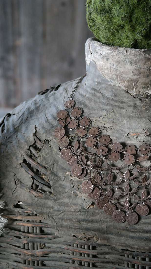 Sierketting met roestkleurige muntjes en bloemvormige hangers, De Hooyzolder, gedrapeerd over een sculptuur