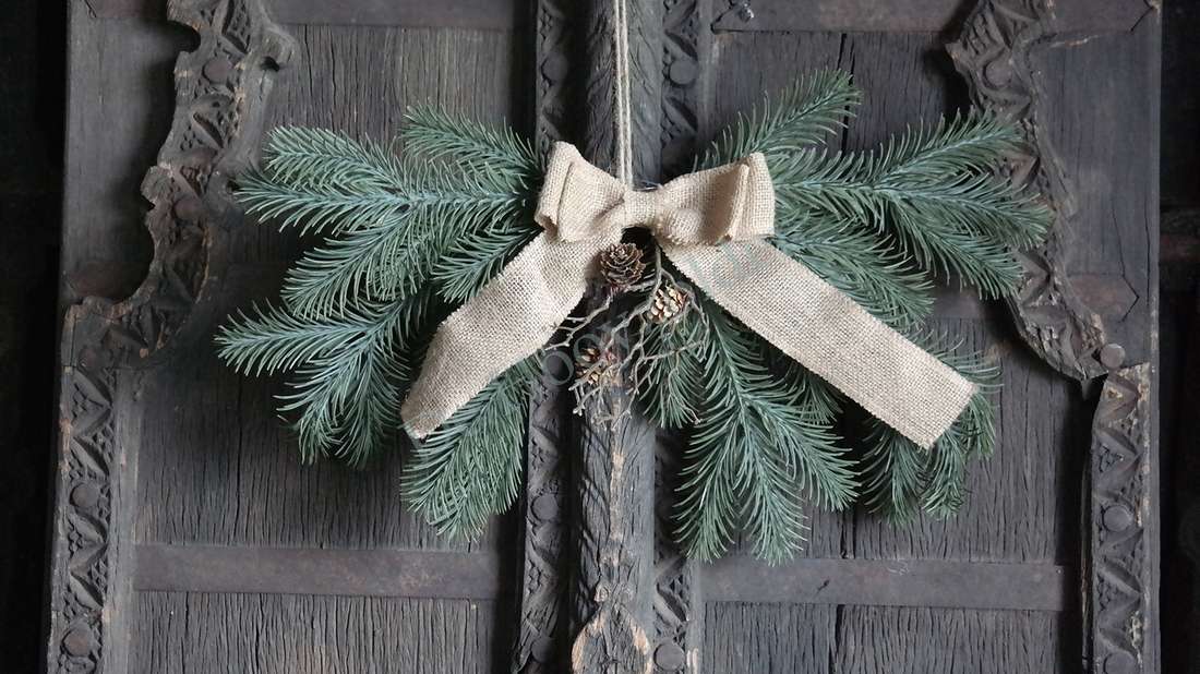 Hanger dennentakken real touch met strik, groene dennentakken en een burlap-strik op donker houten deur