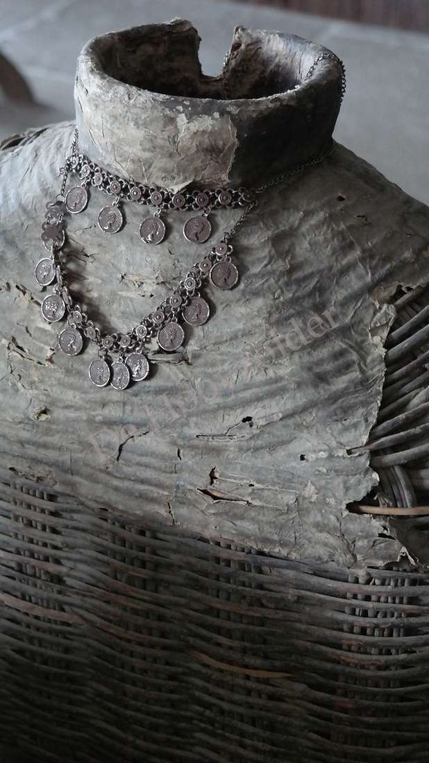Een decoratieve sierketting met muntjes in zilver metaal om een grijze buste.