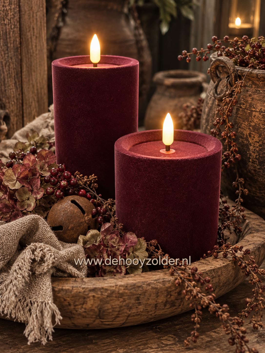 Twee velvet stompkaarsen donkerbruin/bordeaux, brandend, in houten schaal met droogbloemen; De Hooyzolder