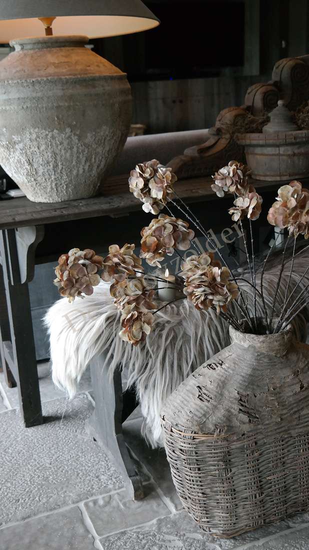 Gedroogde hortensia, zes bloemen in beige-bruin, in een rieten vaas op een houten tafel