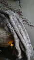 Plaid Iza imitatiebont - bruin mix, grijsbruine vacht over rieten mand met kaars, De Hooyzolder