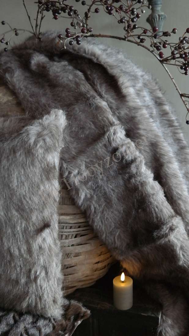 Plaid Iza imitatiebont bruin mix, gedrapeerd over een rieten mand met een brandende kaars ernaast