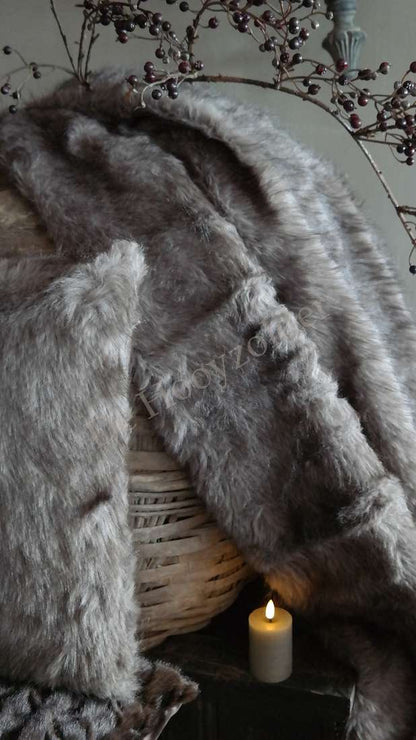 Plaid Iza imitatiebont bruin mix, gedrapeerd over een rieten mand met een brandende kaars ernaast