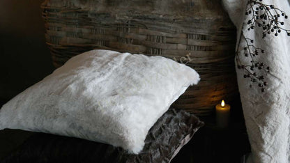 Kussen Zaya bont créme, wit-creme faux fur kussen op wicker achtergrond bij een brandende kaars