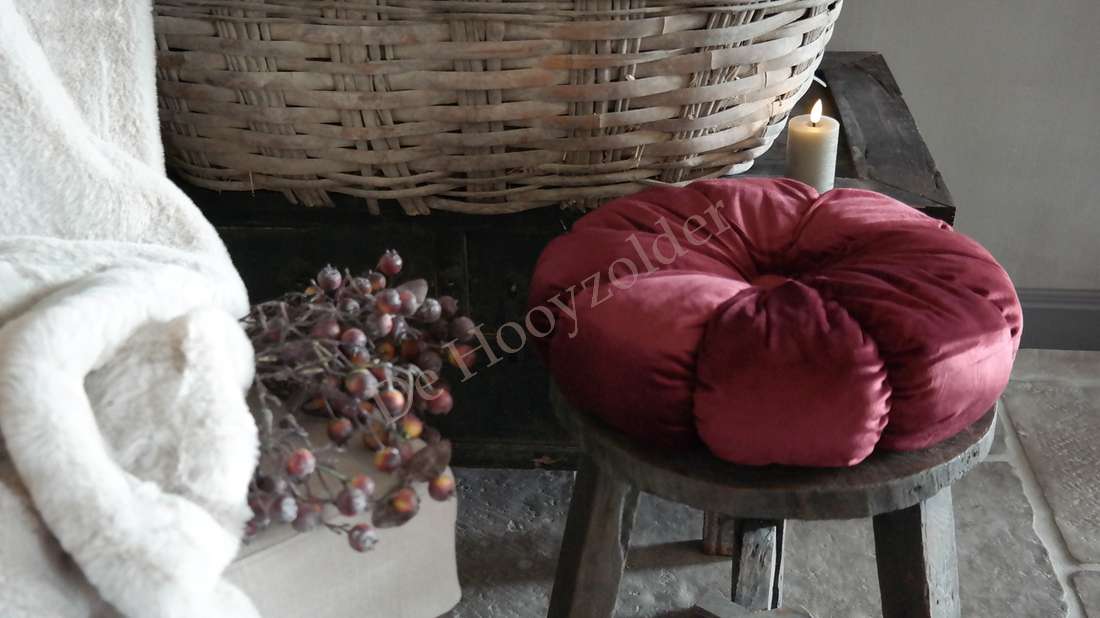 Kussen rond velvet bordeaux van De Hooyzolder op houten kruk, naast mand, kaars en gedroogde bessen
