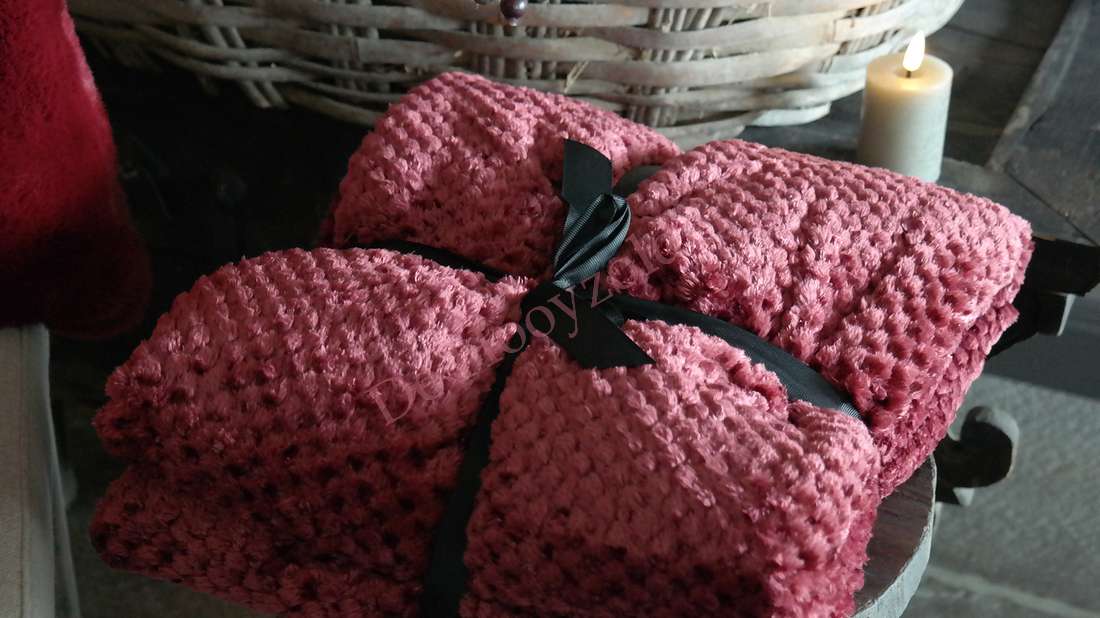 Plaid Rick fluffy - bordeaux, twee bordeauxkleurige plaids met zwarte linten op een houten tafel naast een kaars.
