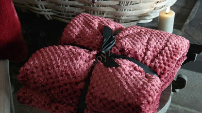 Plaid Rick fluffy - bordeaux, twee bordeauxkleurige plaids met zwarte linten op een houten tafel naast een kaars.