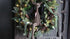 Rendier zittend velvet bruin op groene kerstkrans met dennenappels en lampjes (De Hooyzolder)