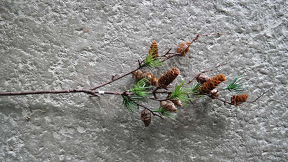Kunsttak met dennenappels en groene naalden aan een bruine tak