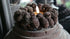 Dennenappelkransje 15 cm met brandende kaars, rondom donkerbruine dennenappels op een houten schijf (De Hooyzolder)