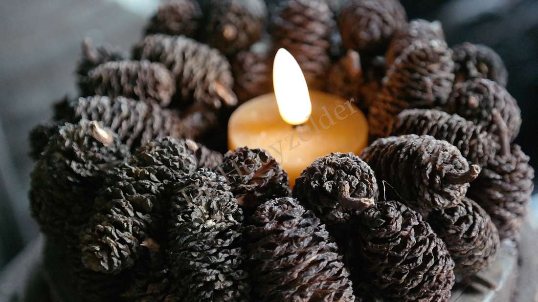 LED-waxinelichtje oranje-bruin tussen dennenappeltjes en een warme gloed