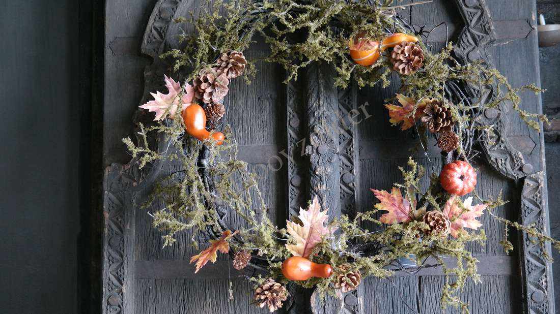 Mos-Herfst krans van De Hooyzolder met mos, dennenappels en oranje herfstvruchten aan een donkere deur