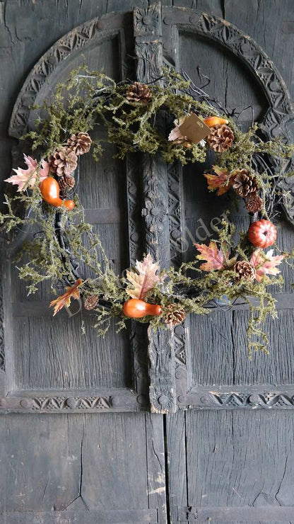 Mos-Herfst krans van De Hooyzolder met dennenappels, oranje pompoenen en mos aan een houten deur.