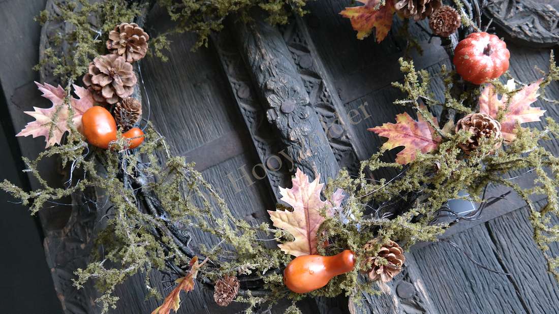 Mos-herfst krans met mos, dennenappels, gedroogde bladeren en oranje pompoentjes aan een houten deur De Hooyzolder