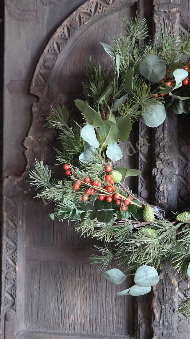 Kerstkrans met eucalyptus en rode bessen, dennennaalden, op houten achtergrond
