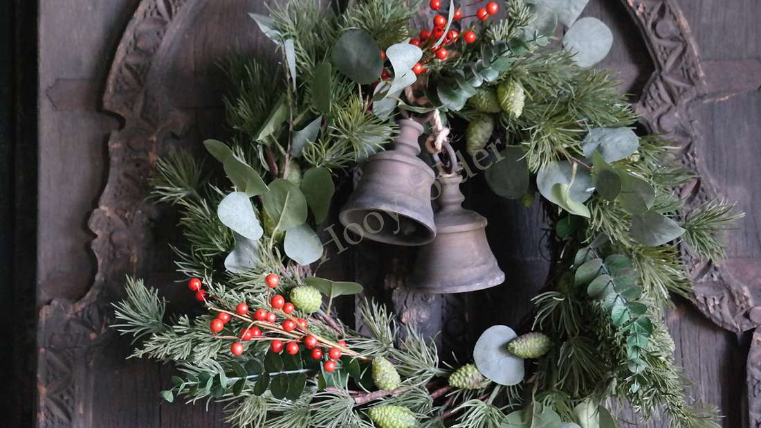 Kerstkrans De Hooyzolder met eucalyptus, rode bessen en groene takken met twee metalen bellen, op een houten achtergrond