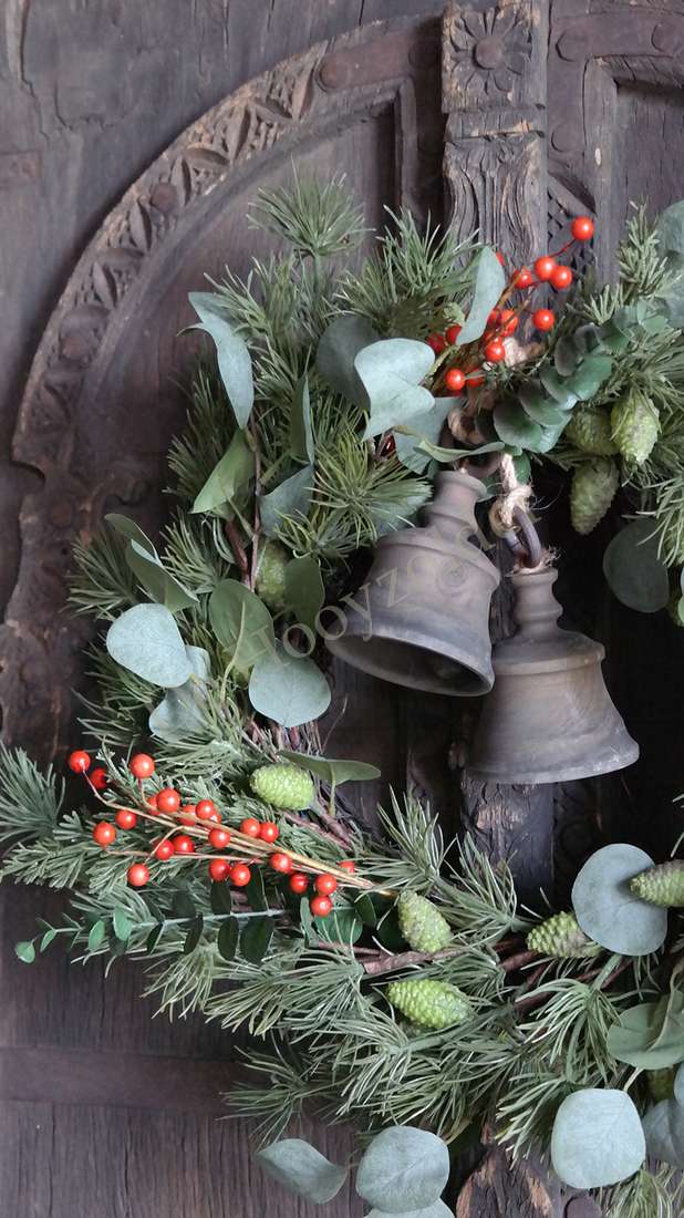 Kerstkrans met eucalyptusbladeren en rode bessen, twee metalen belletjes tegen een donker houten achtergrond