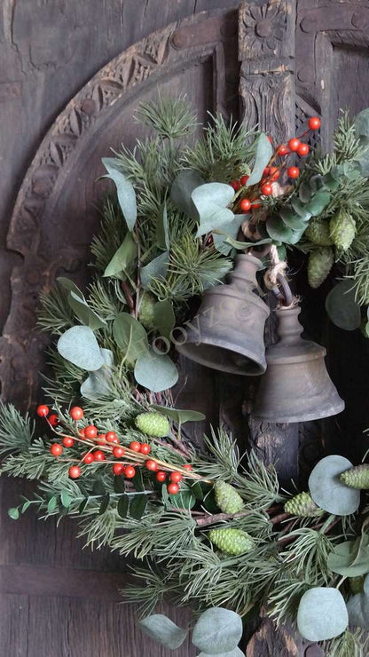 Kerstkrans met eucalyptusbladeren en rode bessen, twee metalen belletjes tegen een donker houten achtergrond