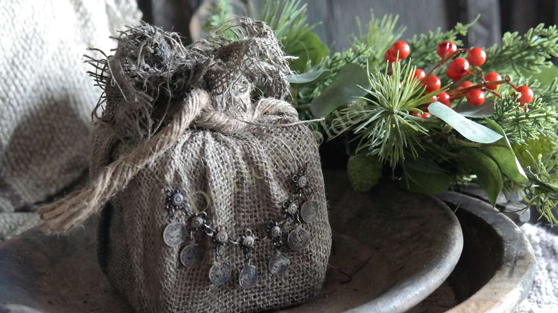 Jute cadeau met ketting; sober bruine jutezak met ronde muntjeshangers, naast groene takken en rode bessen.