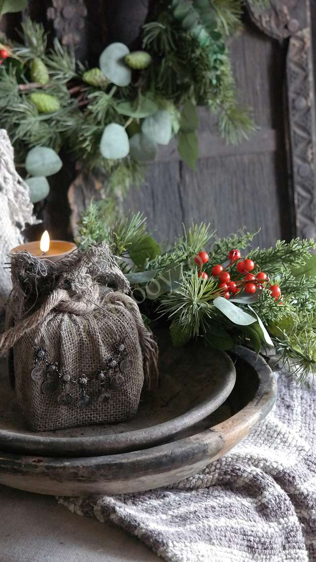 Jute cadeau met ketting, sober bruin, op ronde schaal met groen takken en rode bessen bij een brandende kaars