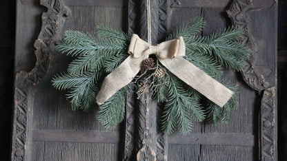 Hanger dennentakken real touch met strik, groene dennentakken en een burlap-strik op donker houten deur