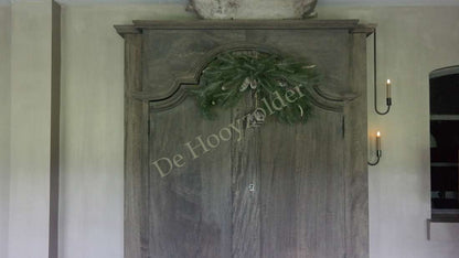 Hanger dennen/pinus real touch 80 cm met groene takken en dennenappels boven een houten kast - De Hooyzolder
