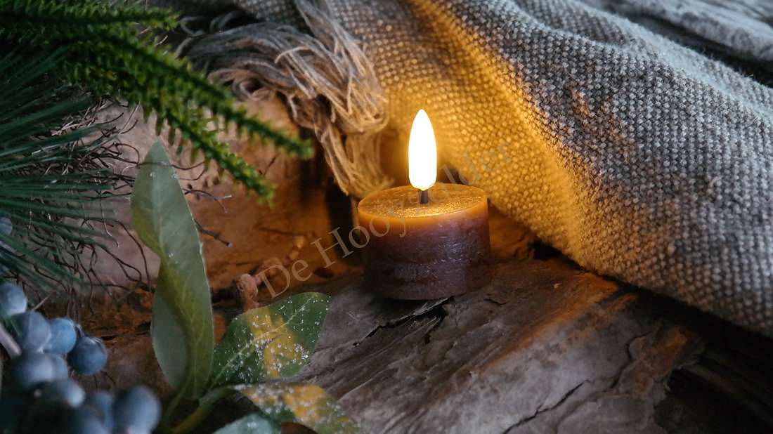 LED-waxinelichtjes bruin op houten ondergrond, aangestoken met warme vlam, omgeven door textiel en groen decor