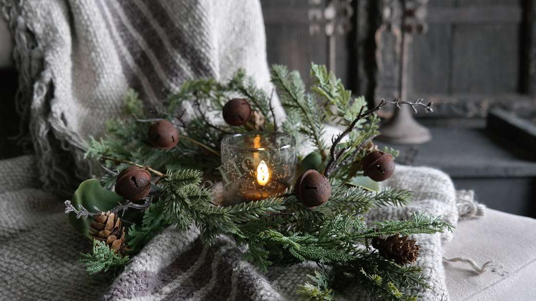 Kerstkrans met groene naalden, dennenappels en bruine bellen rondom glazen kaarsenhouder
