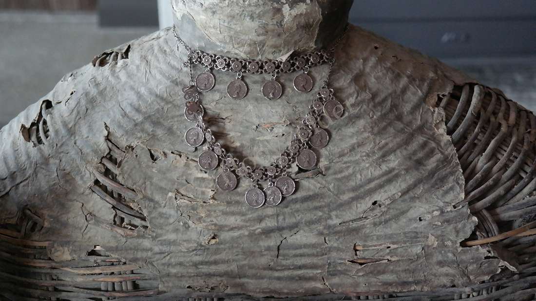 Decoratieve zilveren ketting met muntjes, twee lagen, gedragen op een ruwe gebarsten buste