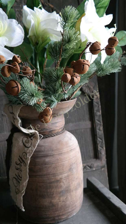 Boeket amaryllis wit in rustieke bruine vaas; groen takken en belletjes, merk De Hooyzolder zichtbaar