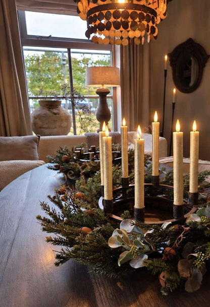 Metalen kaarsenhouder met 8 kaarsen op houten tafel, omgeven door groen en decoratie.